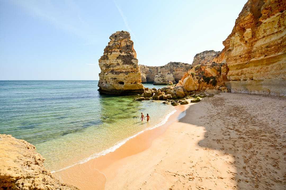 Couple in the water surrounded by limestone cliffs at Praia da Marinha in the Algarve